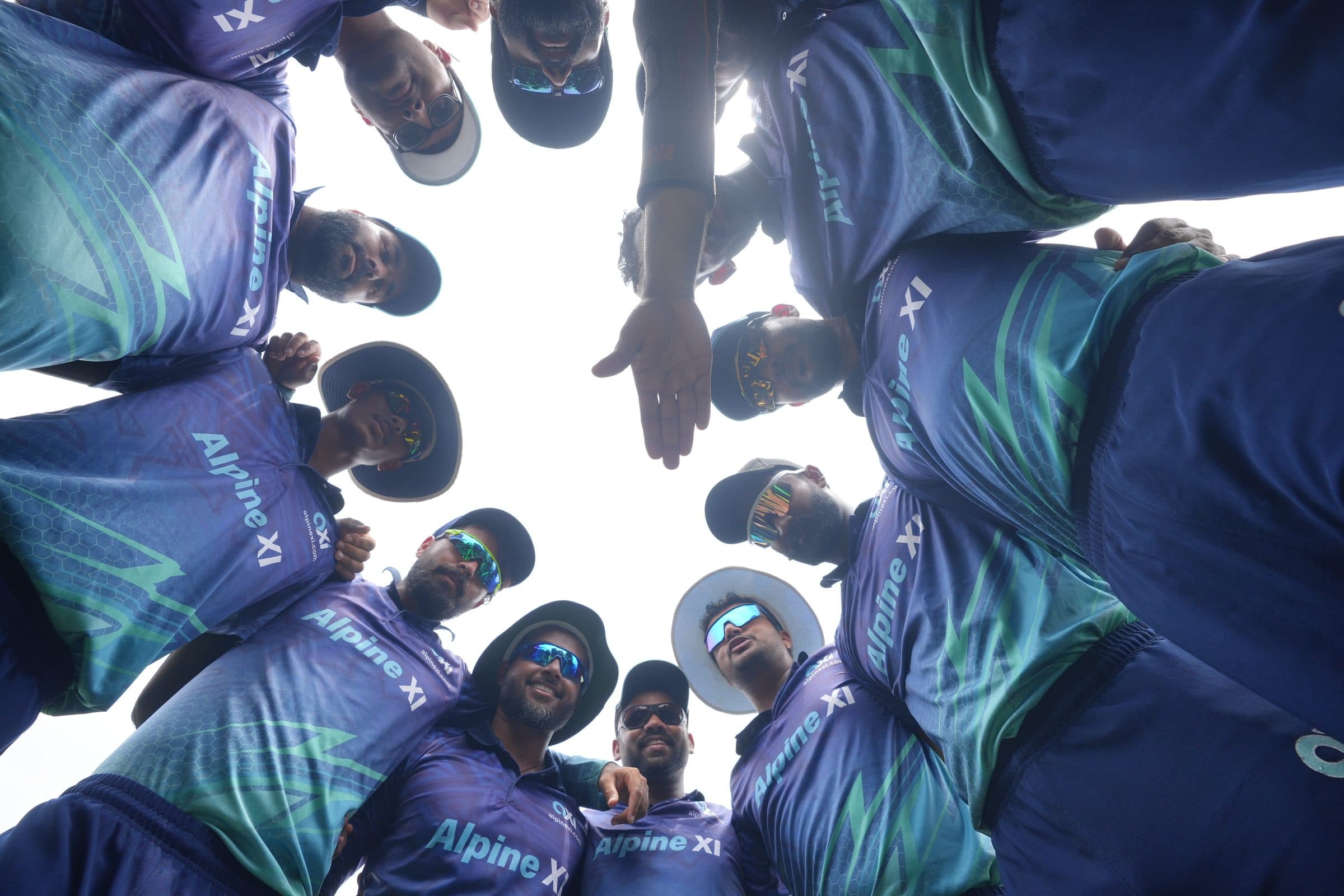 Axi Club players in club kit forming a team huddle, photographed from below against a bright sky