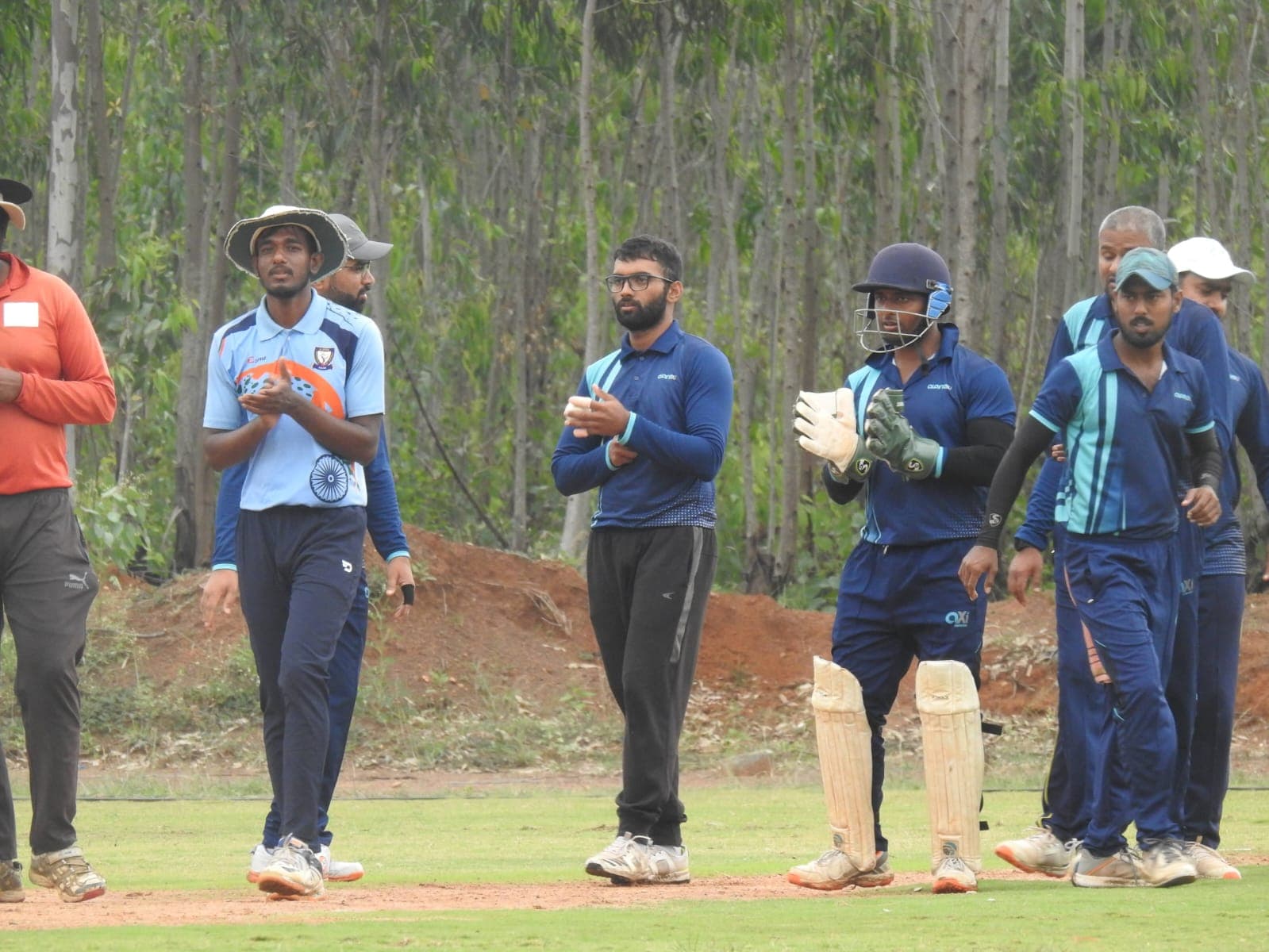 Axi Club fielding side applauding as they walk out, wicket-keeper in pads and gloves