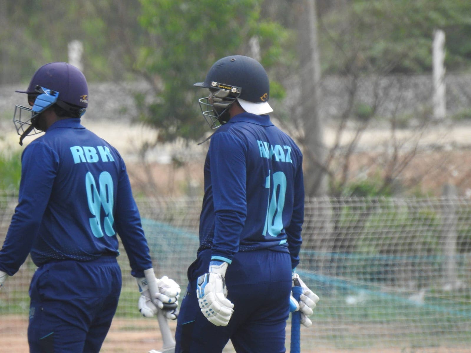Two Axi Club openers in helmets and club kit walking out to bat