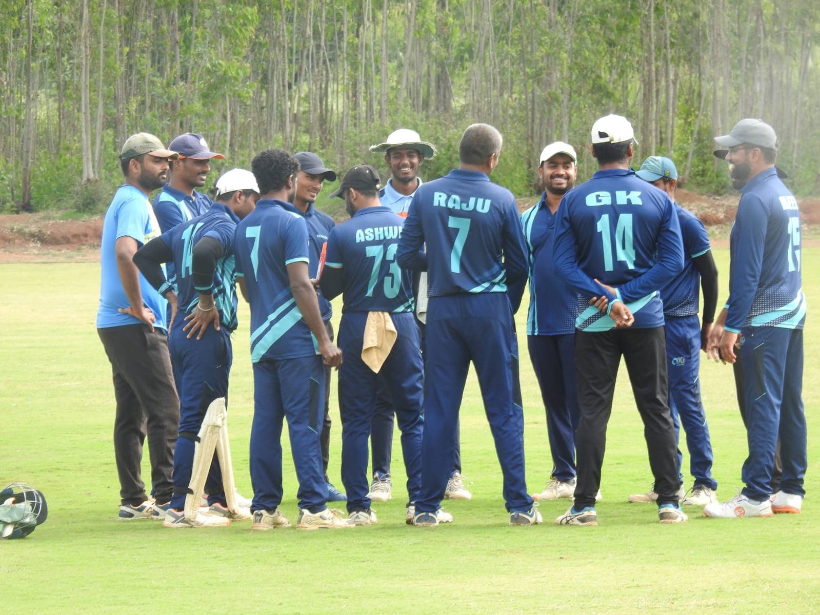 Axi Club fielders in navy and teal club kit gathered in a huddle between overs